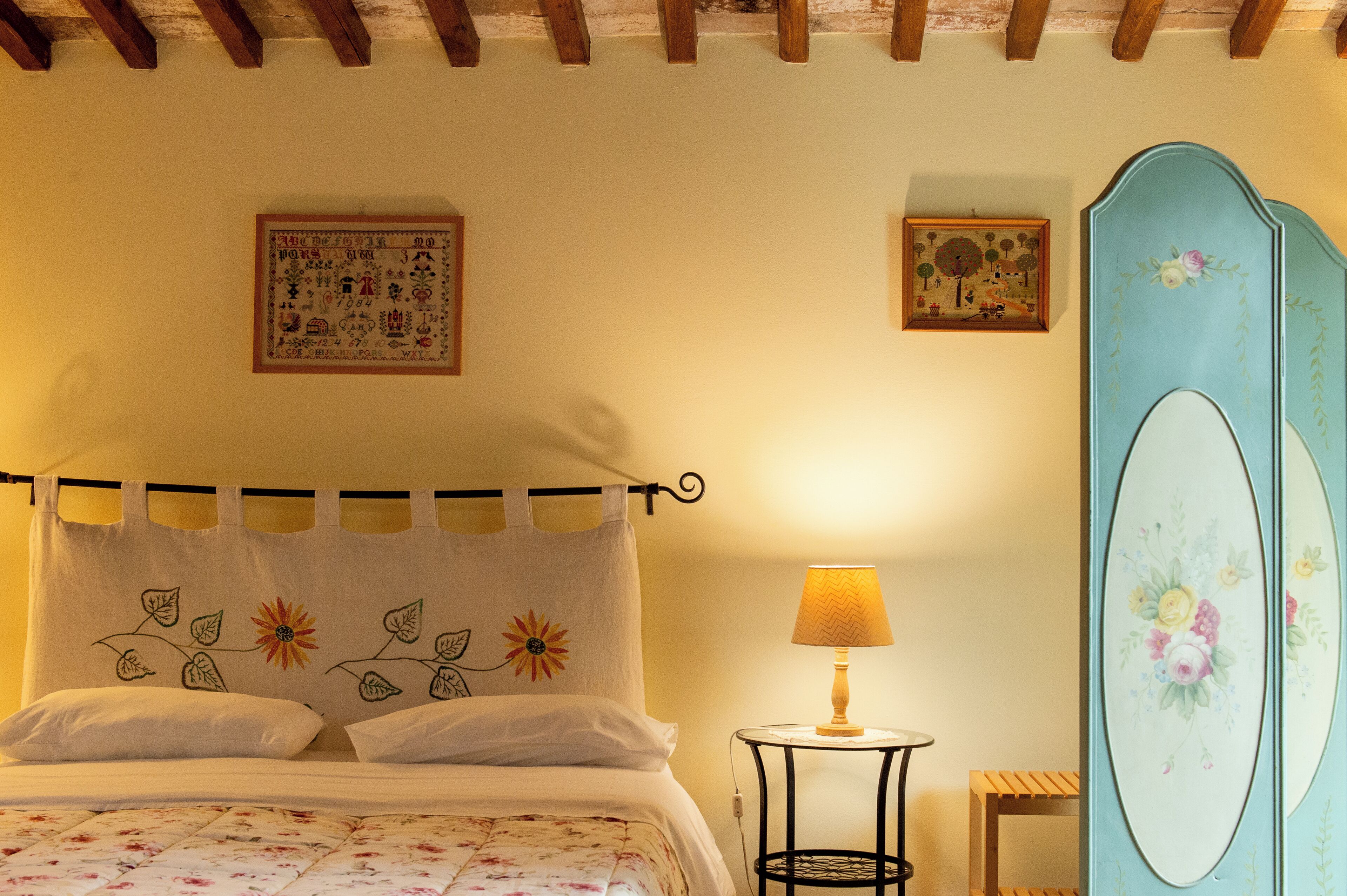 Un dormitorio con una cama, una mesita de noche, una lámpara, un espejo y dos cuadros en la pared.