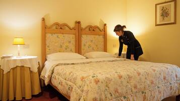 A neatly made bed with a floral bedspread, a bedside table with a lamp, and a framed picture on the wall.