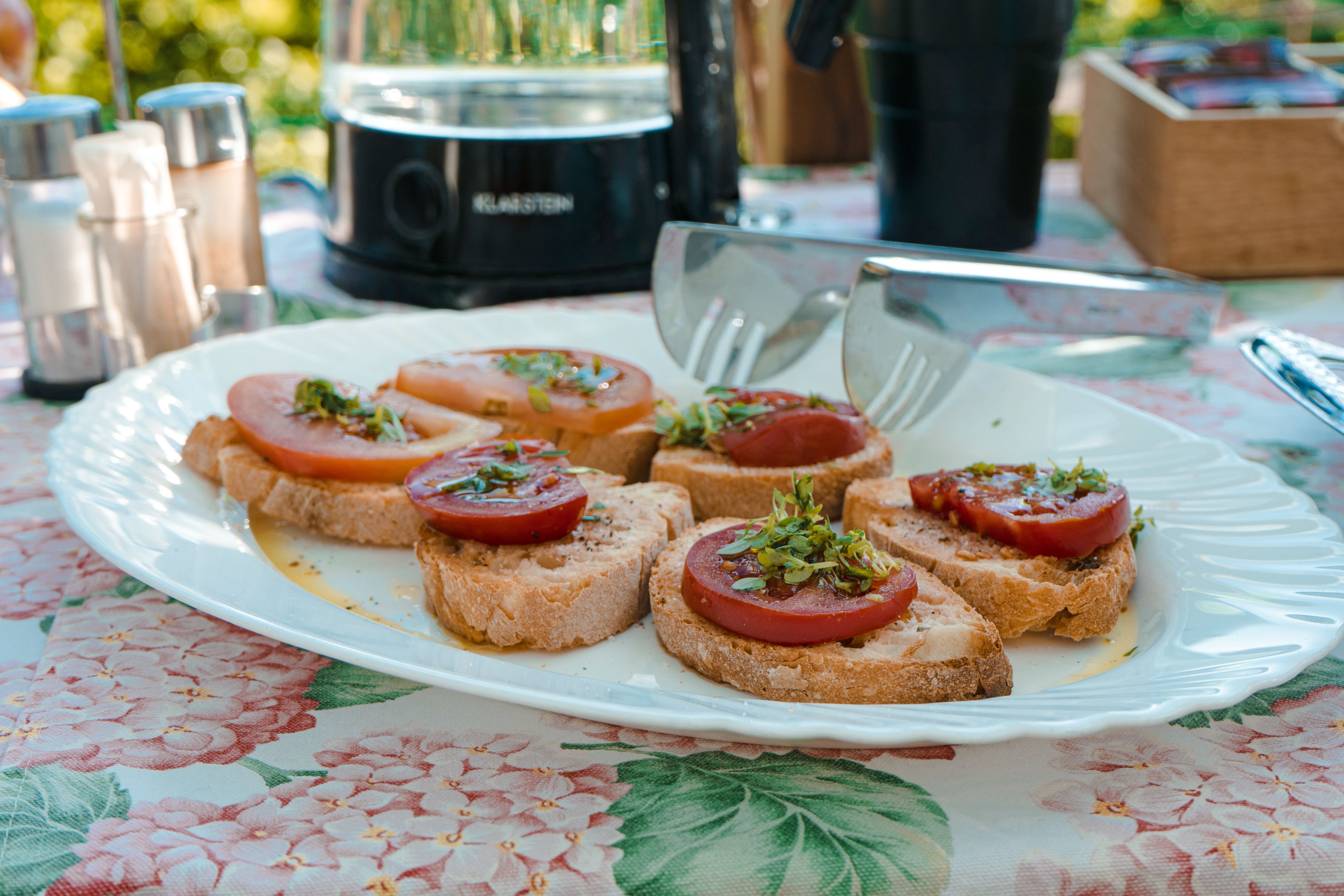 Egy tál bruschetta, paradicsommal és friss fűszernövényekkel, virágmintás terítőn.