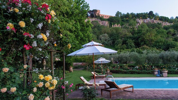 A pool area with lounge chairs and umbrellas, surrounded by lush greenery and flowering plants. - Podere Sette Piagge (Orvieto)