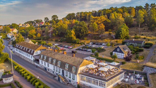 An aerial view of a traditional building with a large patio area, surrounded by parked cars and lush greenery. - Hotel Rusthållargården (Arild)