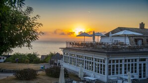 A seaside restaurant with outdoor seating, a view of the ocean, and a building with a balcony overlooking the water. - Hotel Rusthållargården (Arild)