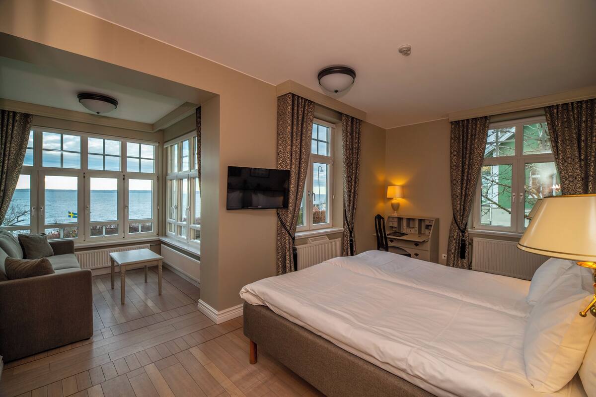 A hotel room with a large bed, a sofa, a TV, and a view of the sea.