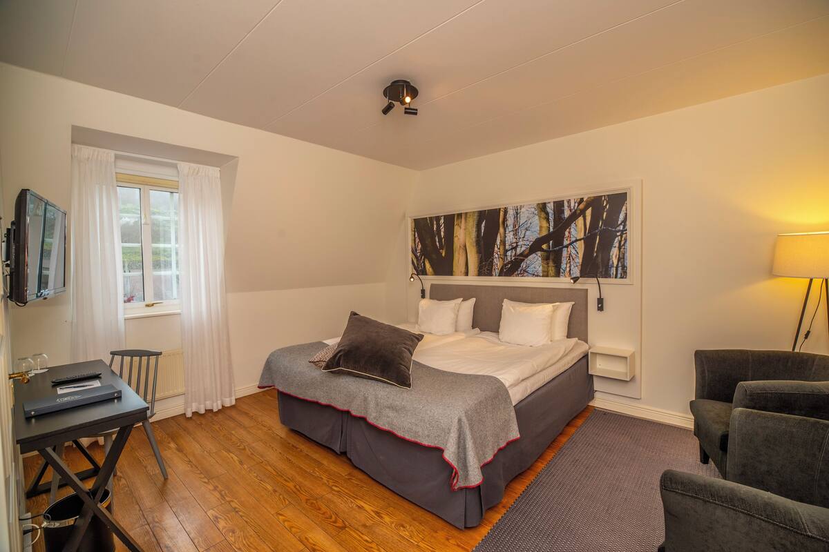 A bedroom with a bed, a desk, a chair, and a painting on the wall.