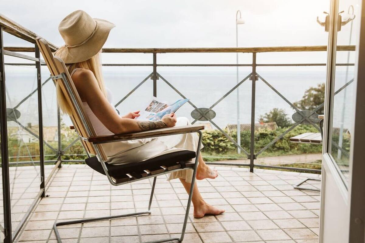 A person sitting on a chair with a view of the sea, reading a book.
