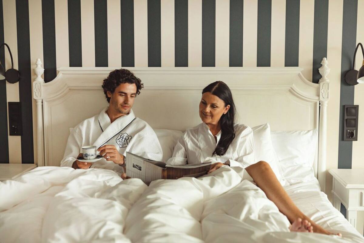 A couple in bed with a striped wall behind them.