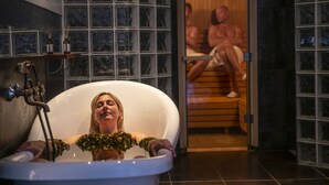 A bathtub with a showerhead, a wooden shelf with bottles, and a tiled wall. - Hotel Rusthållargården (Arild)