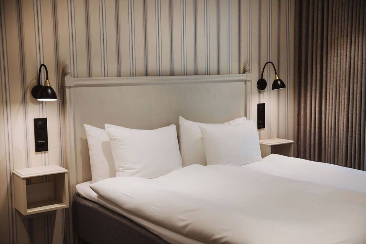 A neatly made bed with white linens and two bedside lamps.