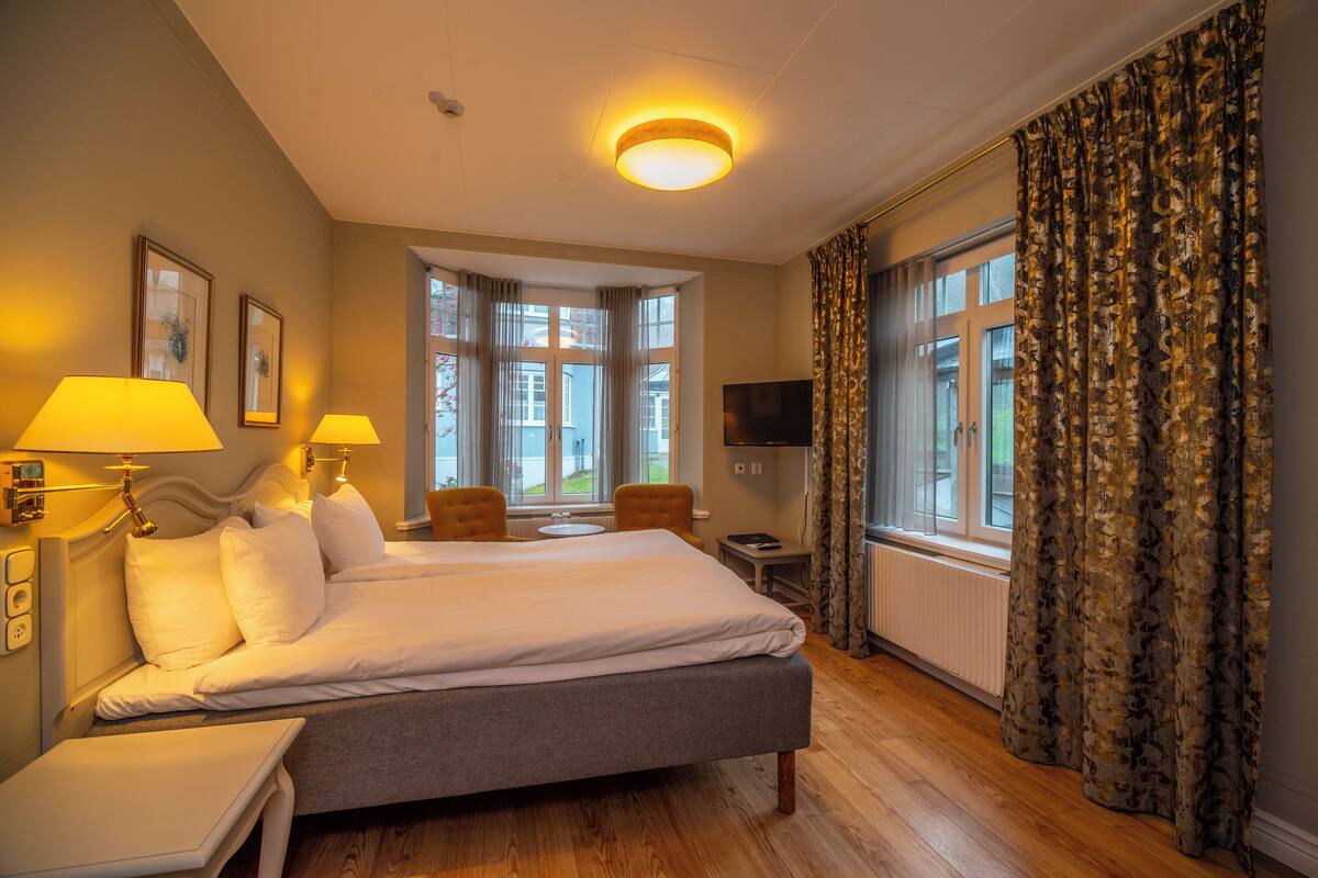 A hotel room with a large bed, two bedside lamps, a TV, a small table, and a chair.