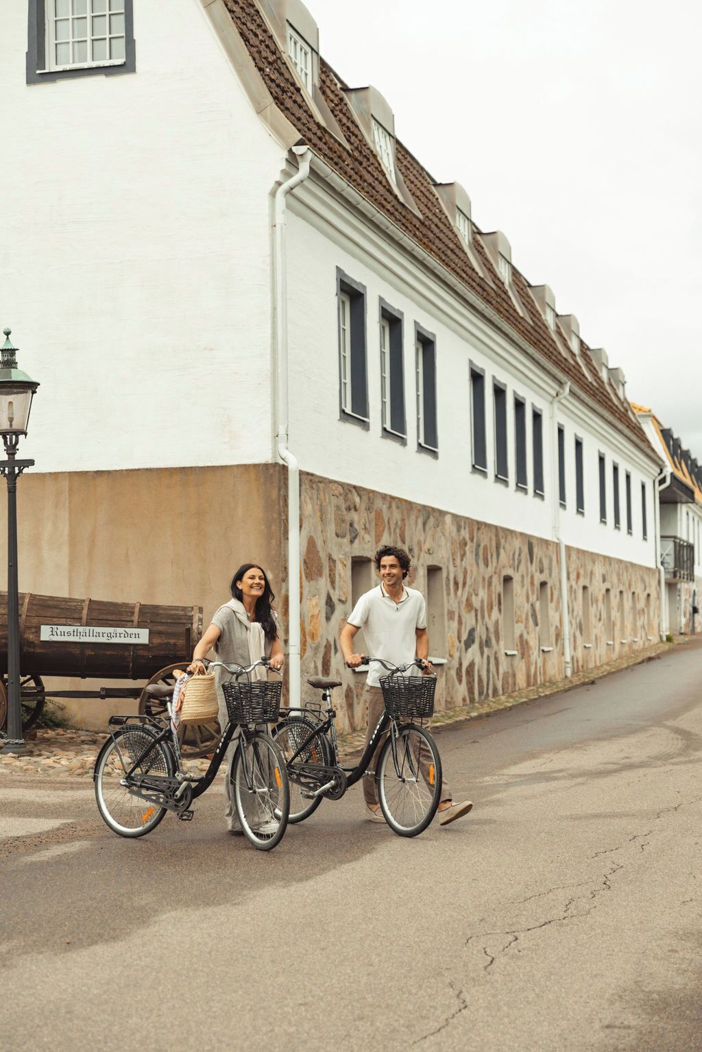 A street with two bicycles parked by a white building with a stone facade.
