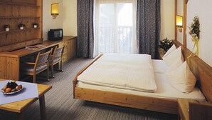 Quarto de hotel com cama de madeira, uma escrivaninha com cadeira, televisão e janela com cortinas.