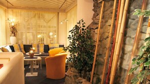 Um lobby de hotel acolhedor com um sofá, poltronas, uma mesinha e uma planta decorativa.