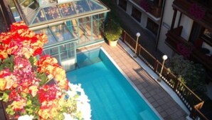 Piscina no terraço com estufa de vidro e flores coloridas.