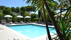 Un espace piscine agrémenté de chaises longues et de parasols, entouré de palmiers et de verdure.
