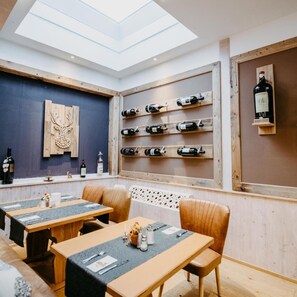 Ein Restaurant mit hoher Decke, Holzwänden und einem Oberlicht. Es gibt mehrere Tische mit Stühlen, und Weinflaschen werden in Regalen präsentiert.