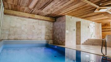 A spa area with a wooden ceiling, a blue pool, and a stone wall.