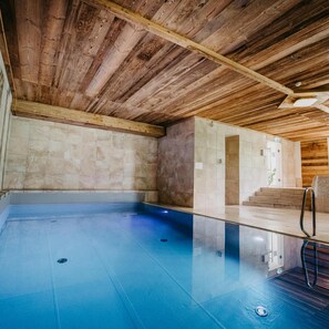 A spa area with a wooden ceiling, a blue pool, and a stone wall.