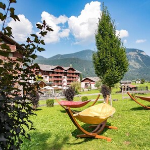 A hotel with multiple buildings, a grassy lawn, and mountains in the background. - Vitalhotel Gosau (Gosau)