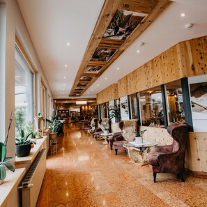Um saguão de hotel com teto de madeira, grandes janelas e área de estar com poltronas confortáveis.
