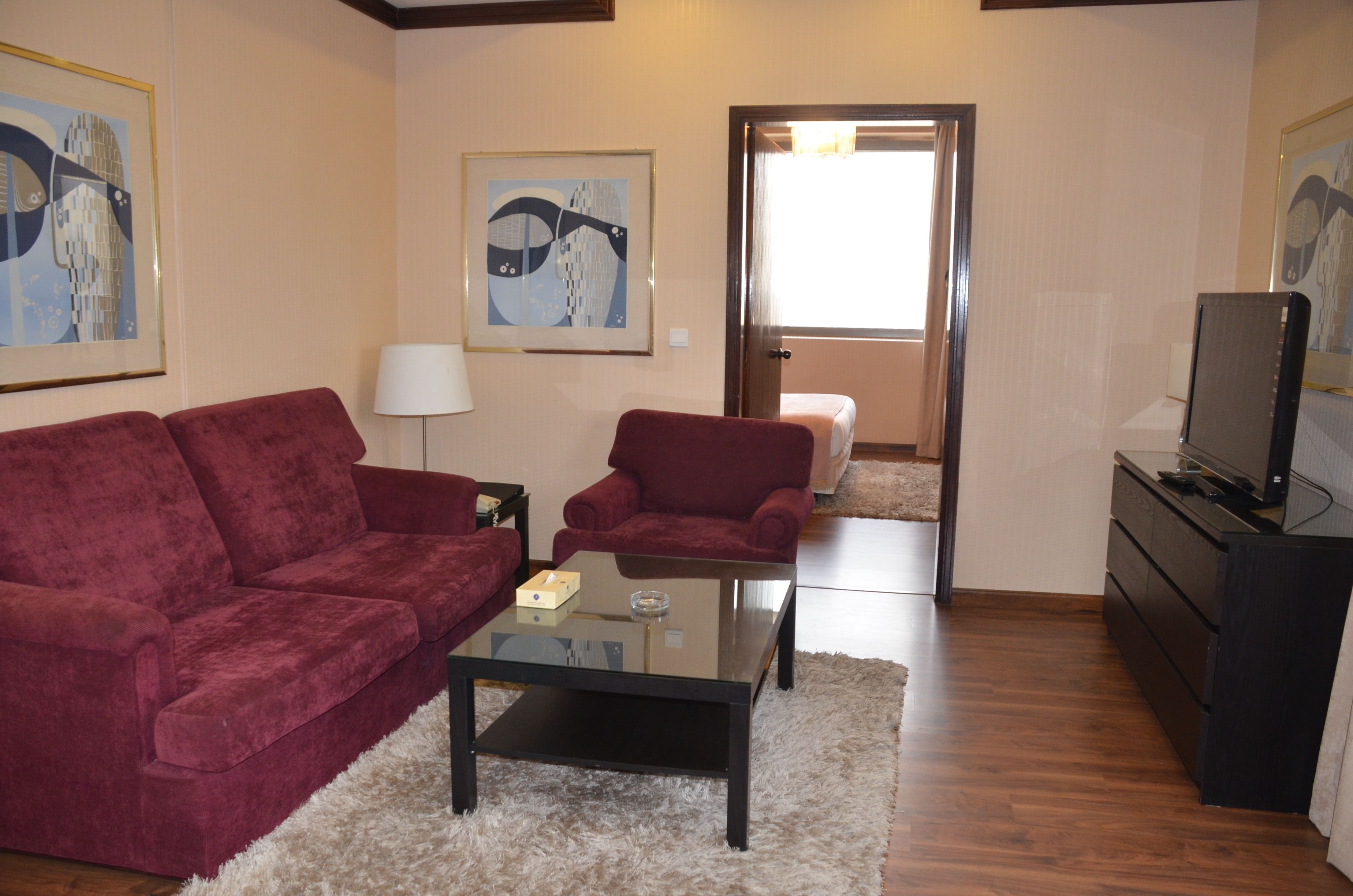 A living room with a red sofa, a glass coffee table, a red armchair, a lamp, a TV, and artwork on the walls.