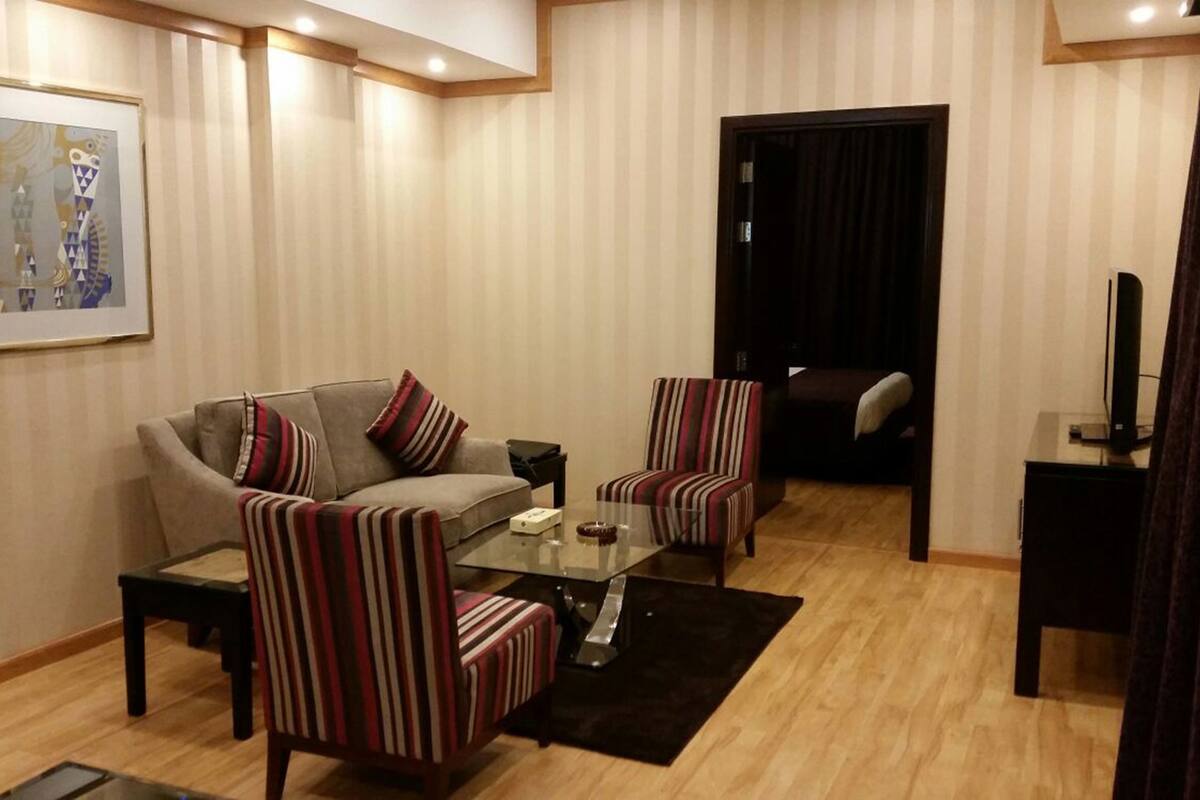 A living room with a sofa, two striped armchairs, a glass coffee table, and a television.