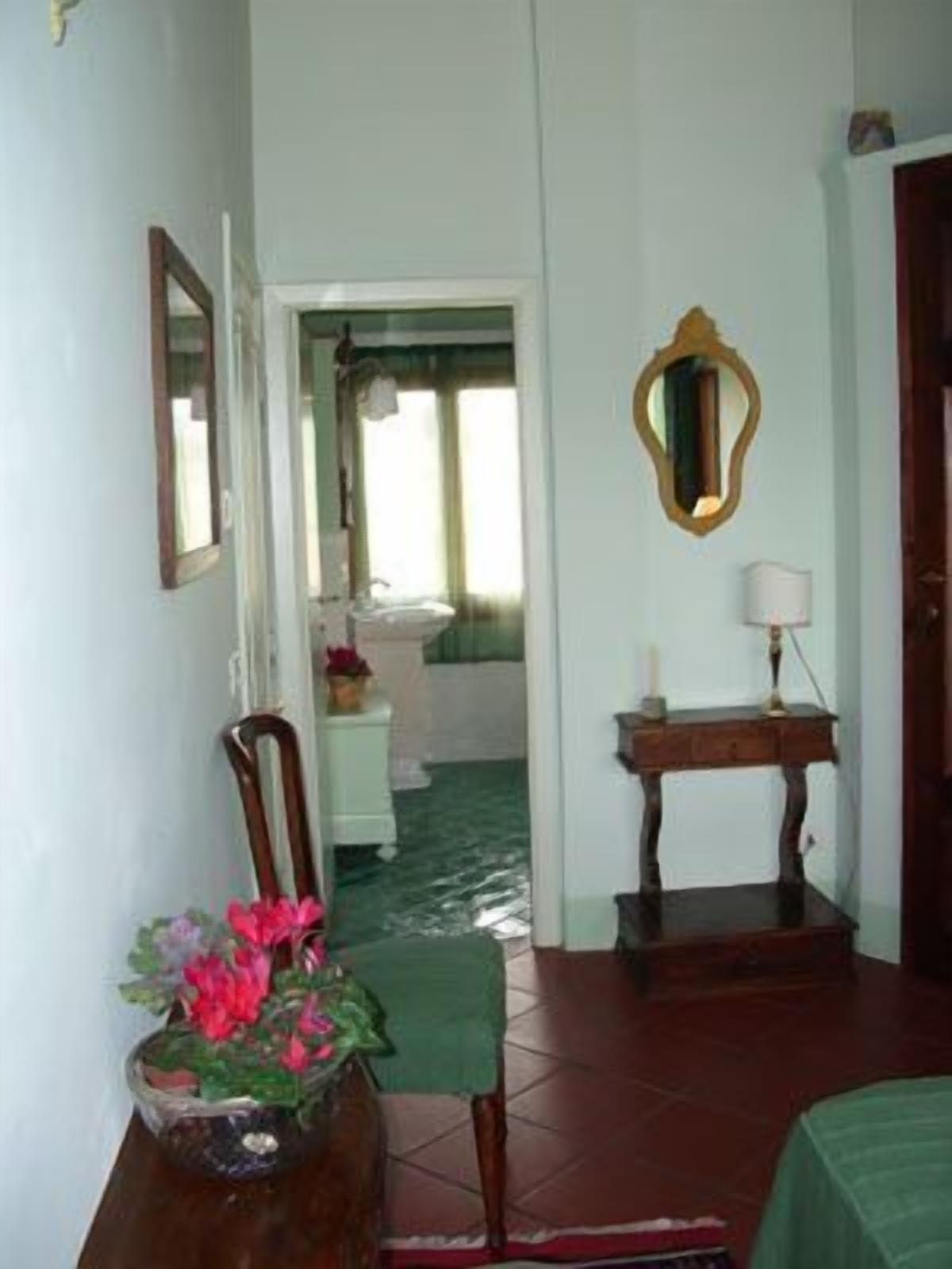 A bedroom with a bed, a chair, a table with a lamp, a mirror, and a window.