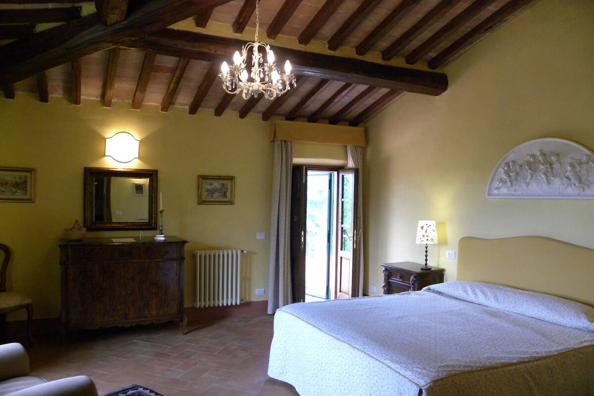 A bedroom with a bed, a dresser, a chair, a radiator, and a chandelier.