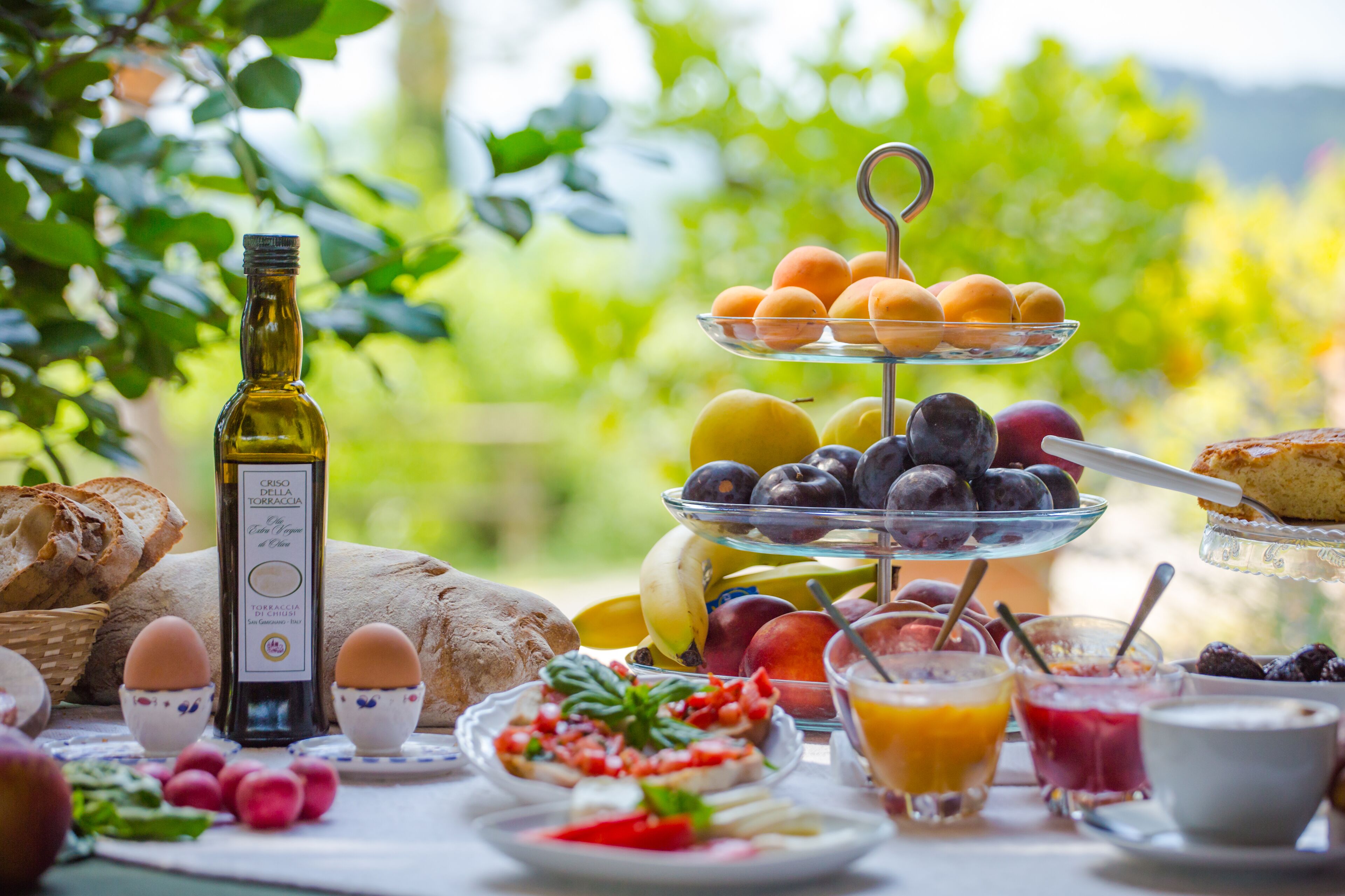 A breakfast table with various foods, including eggs, fruits, bread, and a bottle of olive oil.