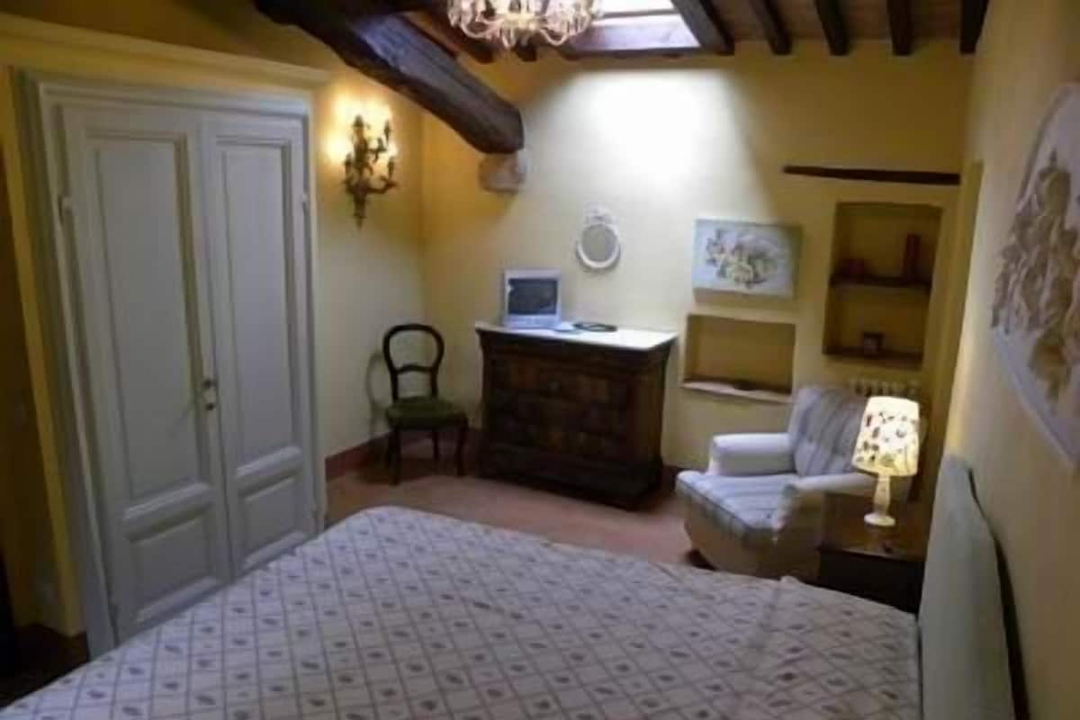 A bedroom with a bed, a dresser, a chair, a desk with a computer, and a lamp.