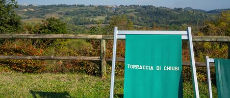 A green sign with the text "TORRACCI DI CHIUSI" on a metal frame, set against a rural landscape with hills and trees.