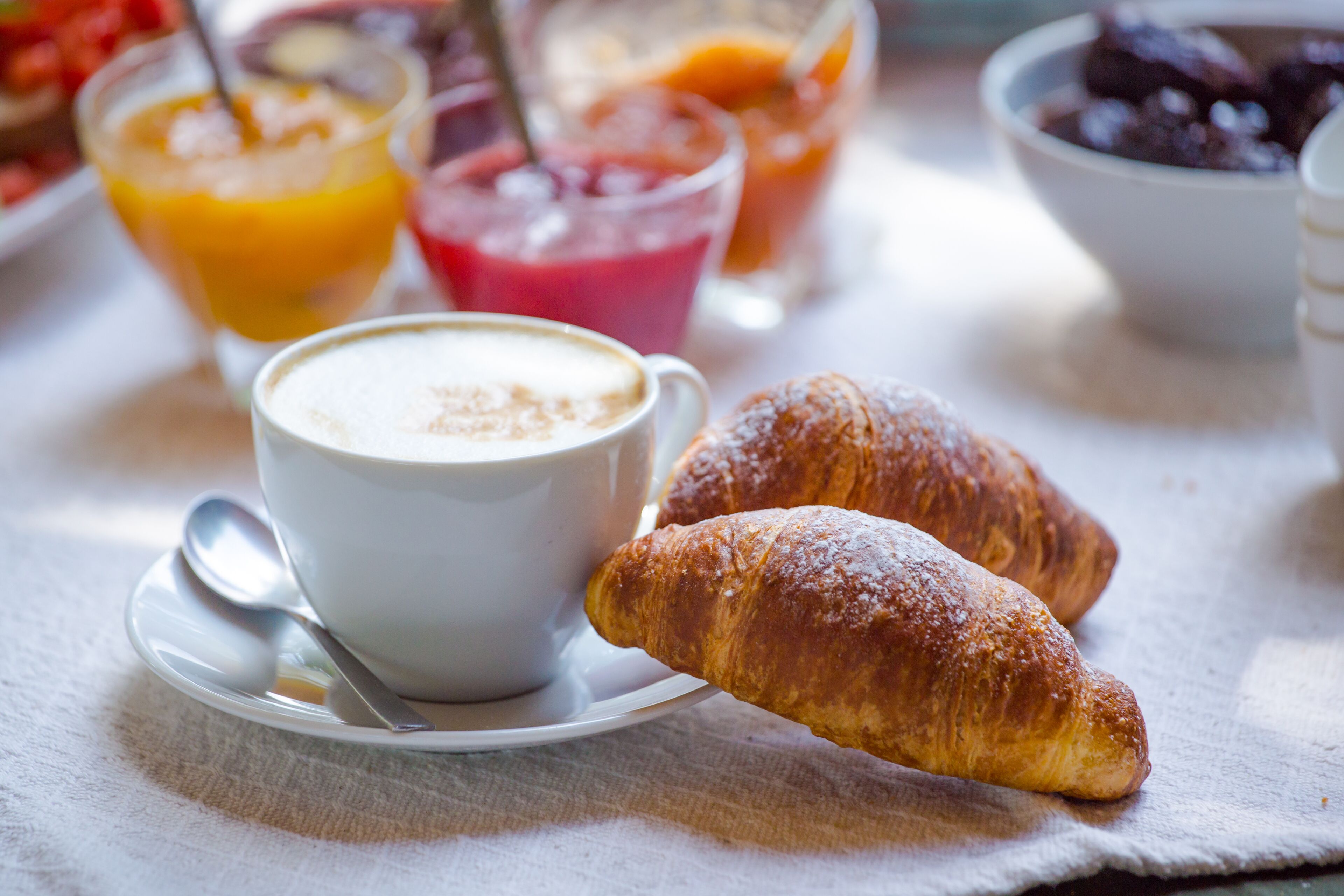 Una mesa con desayuno: una taza de café, un croissant y varios zumos de frutas.