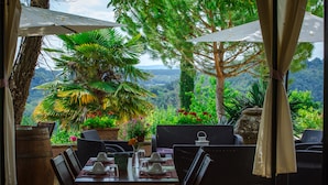 Un área de comedor al aire libre con mobiliario de mimbre, una mesa preparada para dos personas y vistas a un paisaje montañoso.