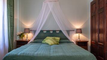 A bedroom with a canopy bed, two bedside tables with lamps, a wooden wardrobe, and a green-striped bedspread.