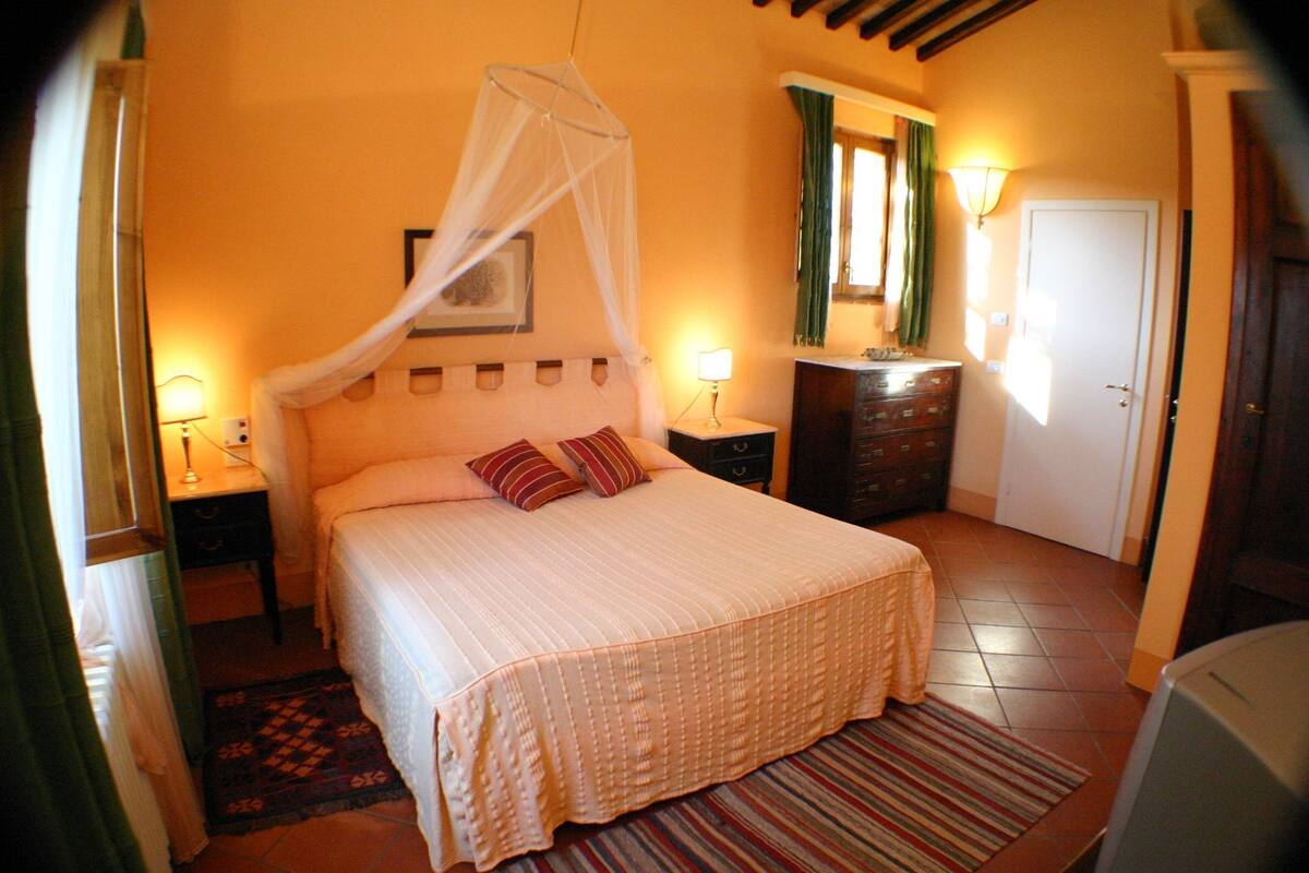 A bedroom with a bed, bedside tables, a nightstand, a dresser, a mirror, a door, and a window with curtains.