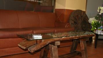 Una mesa de centro de madera con cubierta de vidrio, un sofá de cuero marrón y una rueda decorativa al fondo.