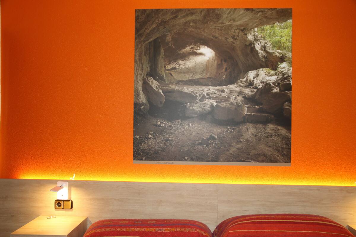 A room with a bed, a nightstand, and a framed picture of a cave.