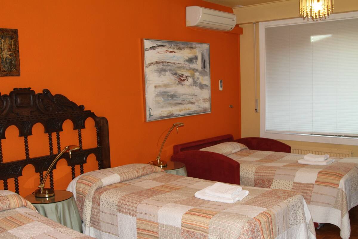 A hotel room with two beds, a wooden headboard, a painting on the wall, and an air conditioning unit.