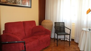 A red sofa, a wicker chair, and a small round table with a remote control. - Hostal Acella (Pamplona)