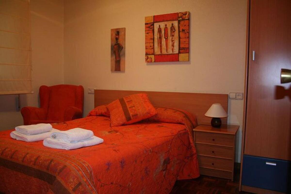A hotel room with a bed, a chair, a nightstand, and artwork on the wall.