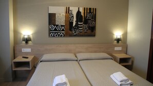 A hotel room with two beds, a wall-mounted artwork, bedside lamps, and a remote control on the nightstand. - Hostal Acella (Pamplona)