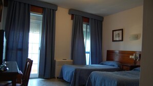 A hotel room with two beds, a wooden headboard, a bedside table with a lamp, a framed picture on the wall, and a window with curtains. - Hotel Marina Victoria (Algeciras)