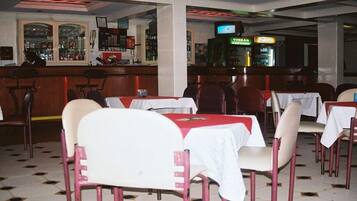 Ein Restaurant mit Tischen, Stühlen, einer Bar und einem Fernsehbildschirm.