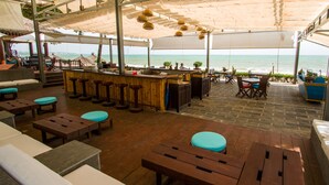 An outdoor seating area with wooden tables and benches, a bar, and a view of the ocean. - Blue Ocean Resort (Mui Ne)