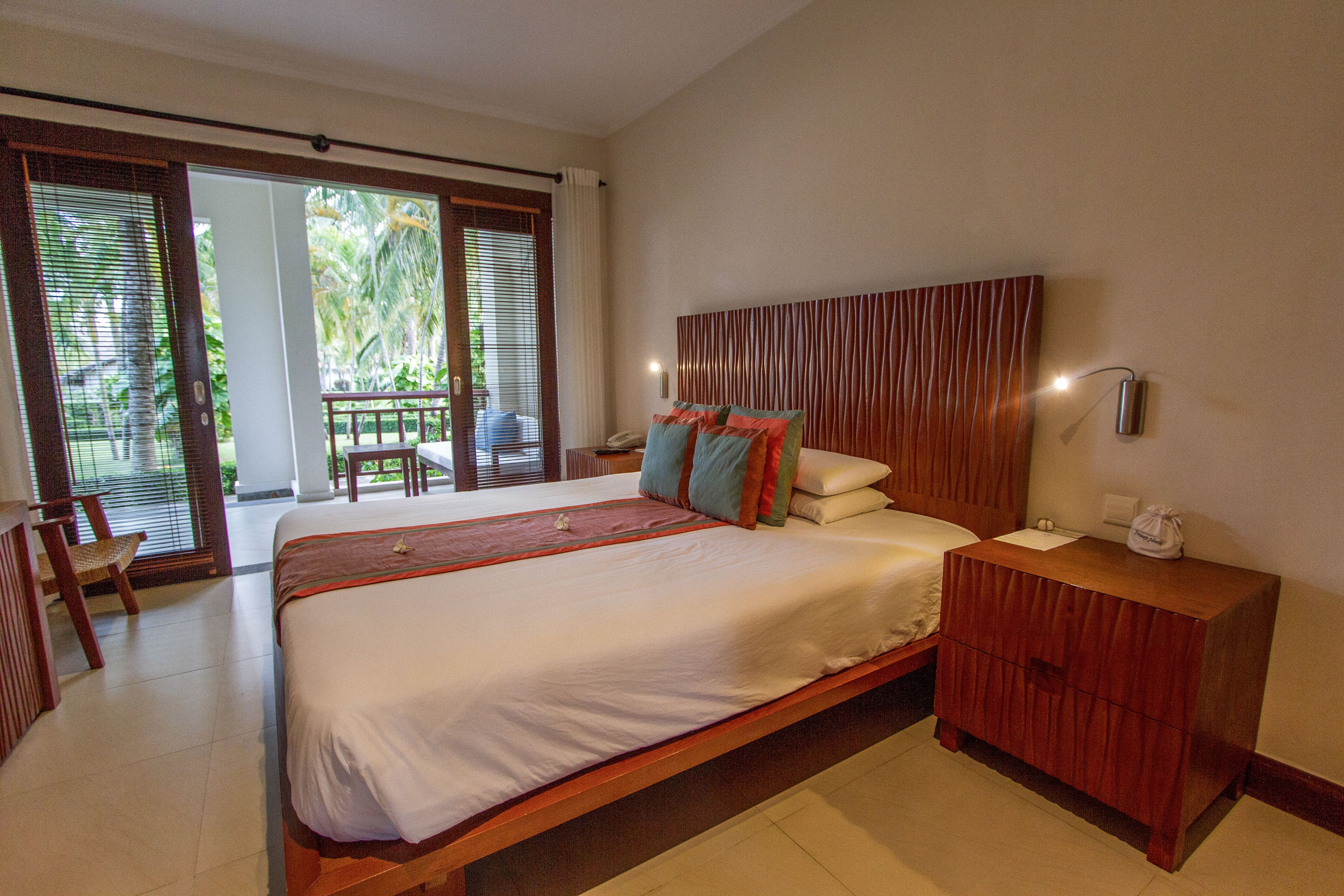 Un dormitorio amplio con una cama grande, una mesita de noche de madera y vistas al exterior a través de una puerta corrediza de vidrio.
