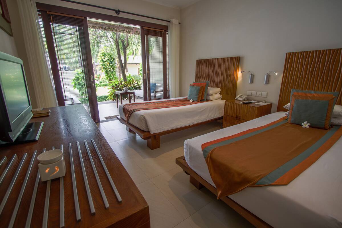 A hotel room with two beds, a desk with a laptop, a chair, and a small table with a candle.