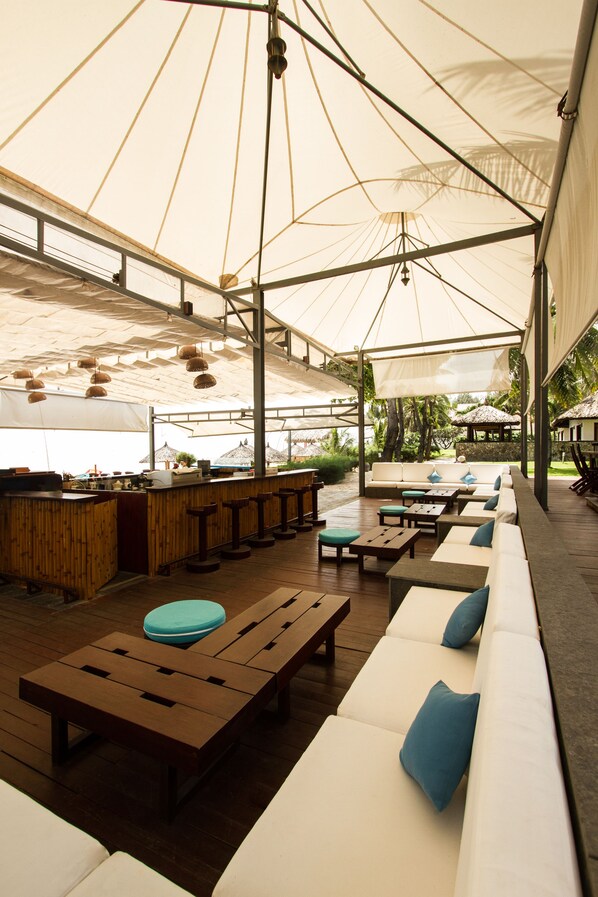 An outdoor seating area with wooden tables and white cushioned sofas, under large white canopies.