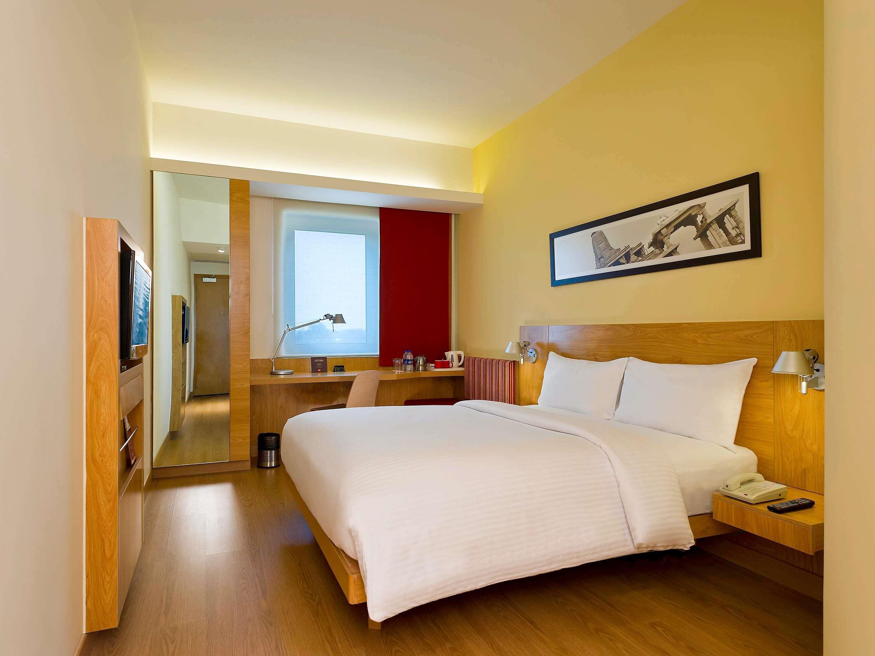 Ein Hotelzimmer mit Bett, Nachttisch, Lampe und Schreibtisch mit Stuhl.