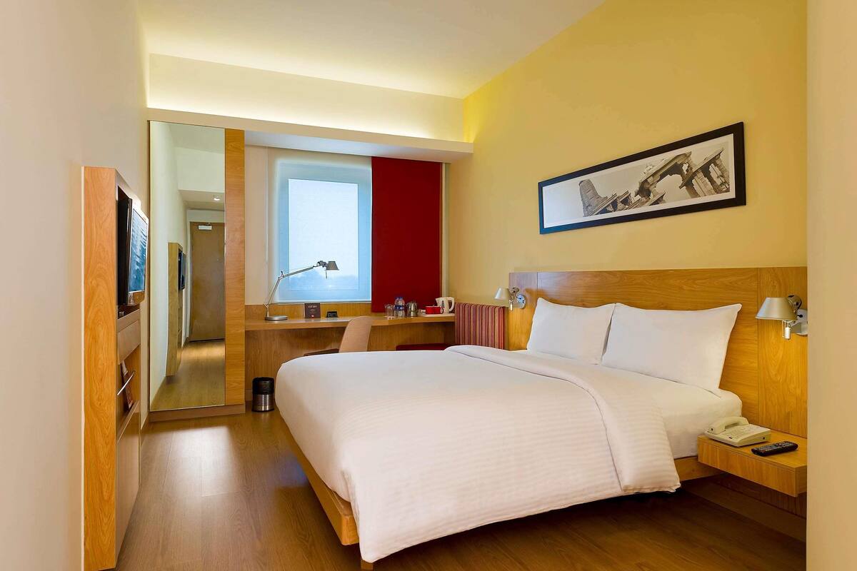 A hotel room with a bed, bedside table, lamp, and a desk with a chair.