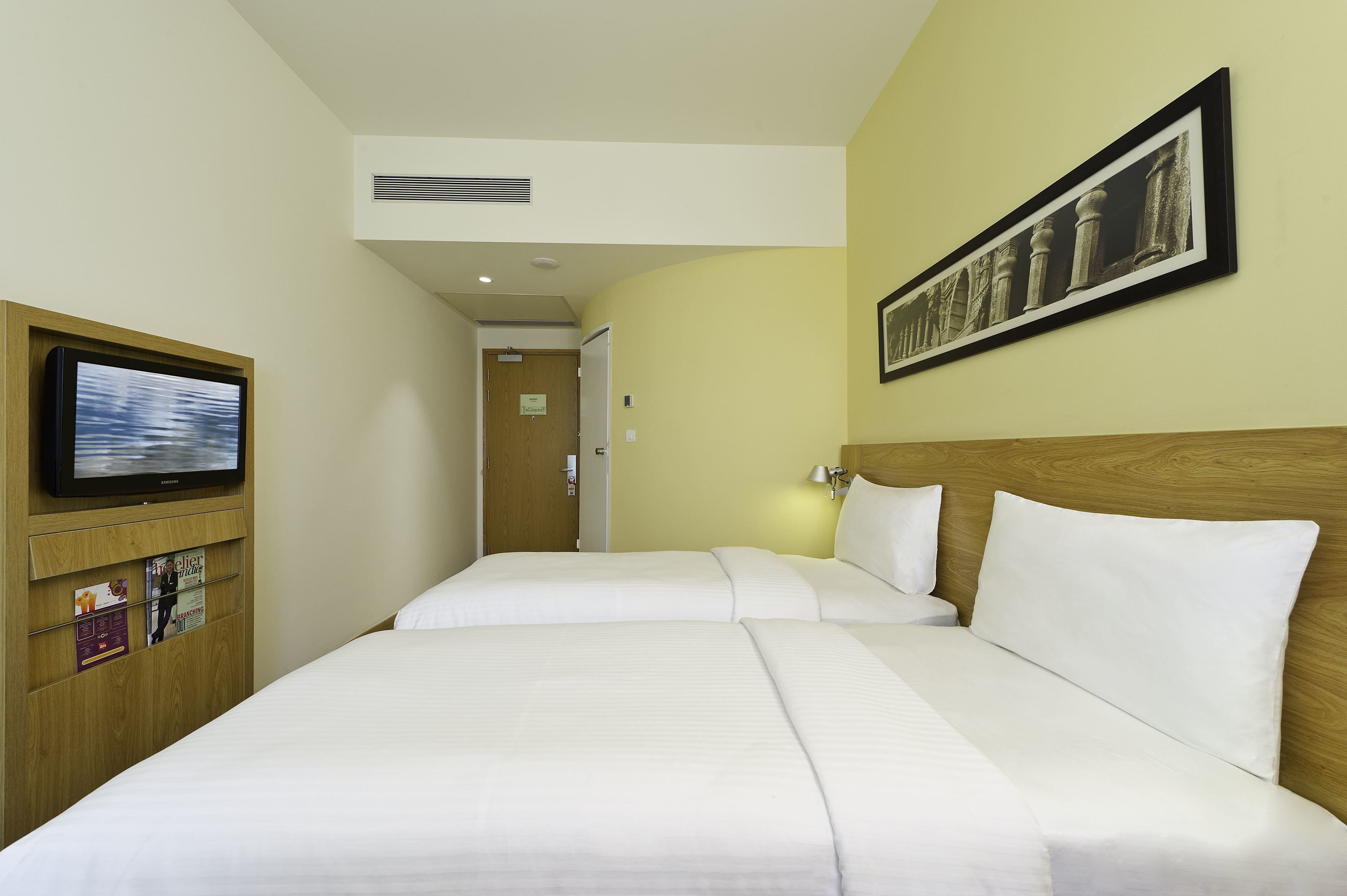 A hotel room with two beds, a television, a framed picture on the wall, and a wooden headboard.