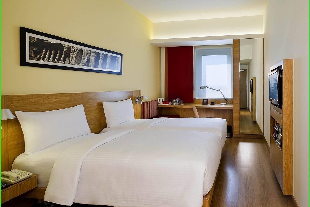 A hotel room with a large bed, a bedside table with a lamp, a TV, and a framed picture on the wall.
